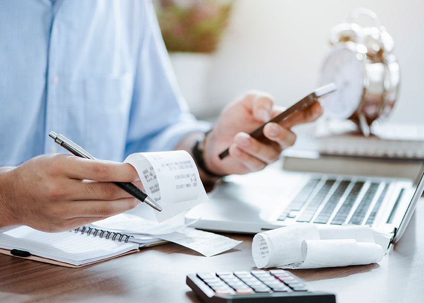 Person's hands holding receipts and pen near a calculator